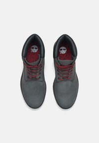 Zapatos de cuero gris con cordones rojos, punta redondeada y acentos negros. La plantilla texturizada presenta un patrón sutil.