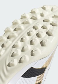 Podešev kopaček na fotbal s texturovaným, světle zbarveným povrchem a několika strategicky rozmístěnými kuželovitými hroty a odolnými bočními prvky.