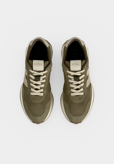 Paire de baskets vert olive et beige avec des lacets blancs et des semelles blanches épaisses, vues de dessus sur un fond uni.
