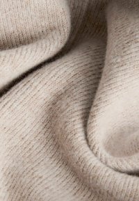 Tessuto lavorato a maglia beige con una superficie morbida e textured. Presenta una fine costina e un aspetto liscio, leggermente peloso.