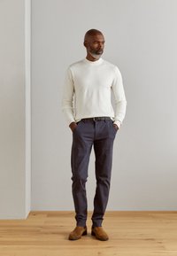 Šviesiai kreminės spalvos, ilgos rankovės megztinis; tamsiai mėlyni, prisitaikantys kelnių; rudi zomšiniai aulinukai iki kulkšnies; minimalistinis dizainas, lygi tekstūra, neutralių atspalvių.