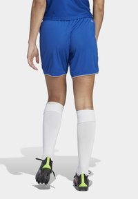 Blauwe sportshorts met witte randen, gecombineerd met witte kniekousen en zwarte voetbalschoenen met neon groene accenten.