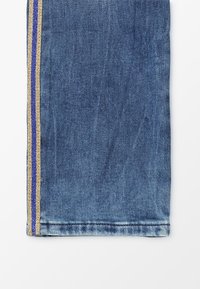 Tela de mezclilla con un tono azul, que presenta un corte recto. Un diseño estrecho de rayas doradas y azules corre verticalmente a lo largo de la costura lateral.