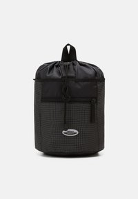 Black drawstring backpack with a grid pattern, featuring a front zip pocket and a logo patch. Made from durable nylon material.