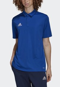Blå polo skjorte lavet af åndbart materiale, med krave, tre knapper og et broderet hvidt adidas-logo på venstre bryst.