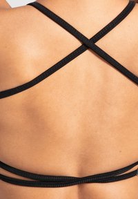 Zwarte sportbeha met meerdere gekruiste banden op de rug, met een gladde textuur en een minimalistisch ontwerp, perfect voor actieve kleding.