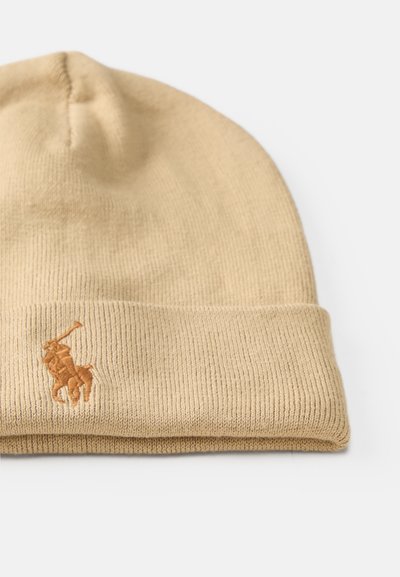 Beige kötött sapka, hajtott mandzsettával és egy kicsit sötétebb árnyalatban hímzett logóval. Simára kötött textura bordás mintával.