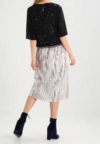 Haut noir à manches courtes avec une jupe plissée texturée argentée, assortis à des bottines bleues. Vue de dos montrant un détail en forme de trou à l'encolure.