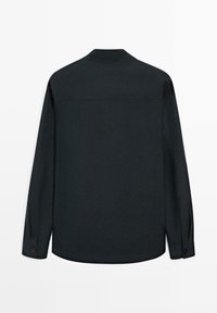 Chemise noire à manches longues avec col classique et poignets boutonnés, vue de dos sur fond blanc.
