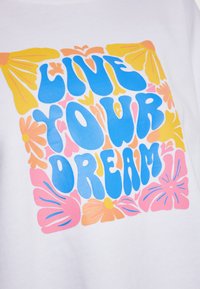 Witte stof met een kleurrafische tekst "LEEF JE DROOM", omringd door bloemenontwerpen in roze, blauw en geel.