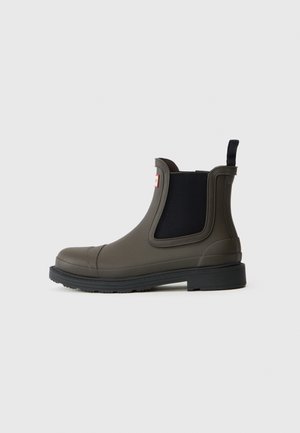 Botte de pluie cheville vert olive avec panneau latéral élastique noir, semelle noire, languette au talon et écusson logo près du haut.
