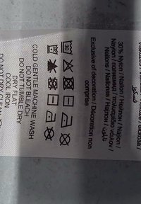 Étiquette d'entretien indiquant la composition du tissu (30 % nylon) et les instructions de lavage : lavage en machine doux à froid, ne pas blanchir, séchage en tambour, séchage à plat, repassage à basse température, pas de nettoyage à sec.