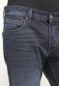 Vaqueros de mezclilla azul oscuro con un corte ajustado, diseño de cinco bolsillos y costuras de contraste. Tela duradera con una textura suave.