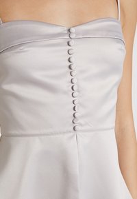 Ljusgrå satin klänning med rak halsringning, featuring en rad av åtta tygklädda knappar längs mitten och tunna axelband.