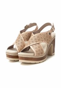 Sandalias de tacón alto en color beige con parte superior perforada, tira ajustable en el tobillo y suela de plataforma texturizada. Detalles en cuero suave.