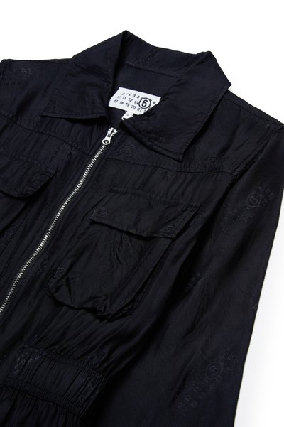 Svart jumpsuit med dragkedja fram, spetsig krage och två bröstfickor. Har en texturerad duk med subtila präglingar och elastisk midja.
