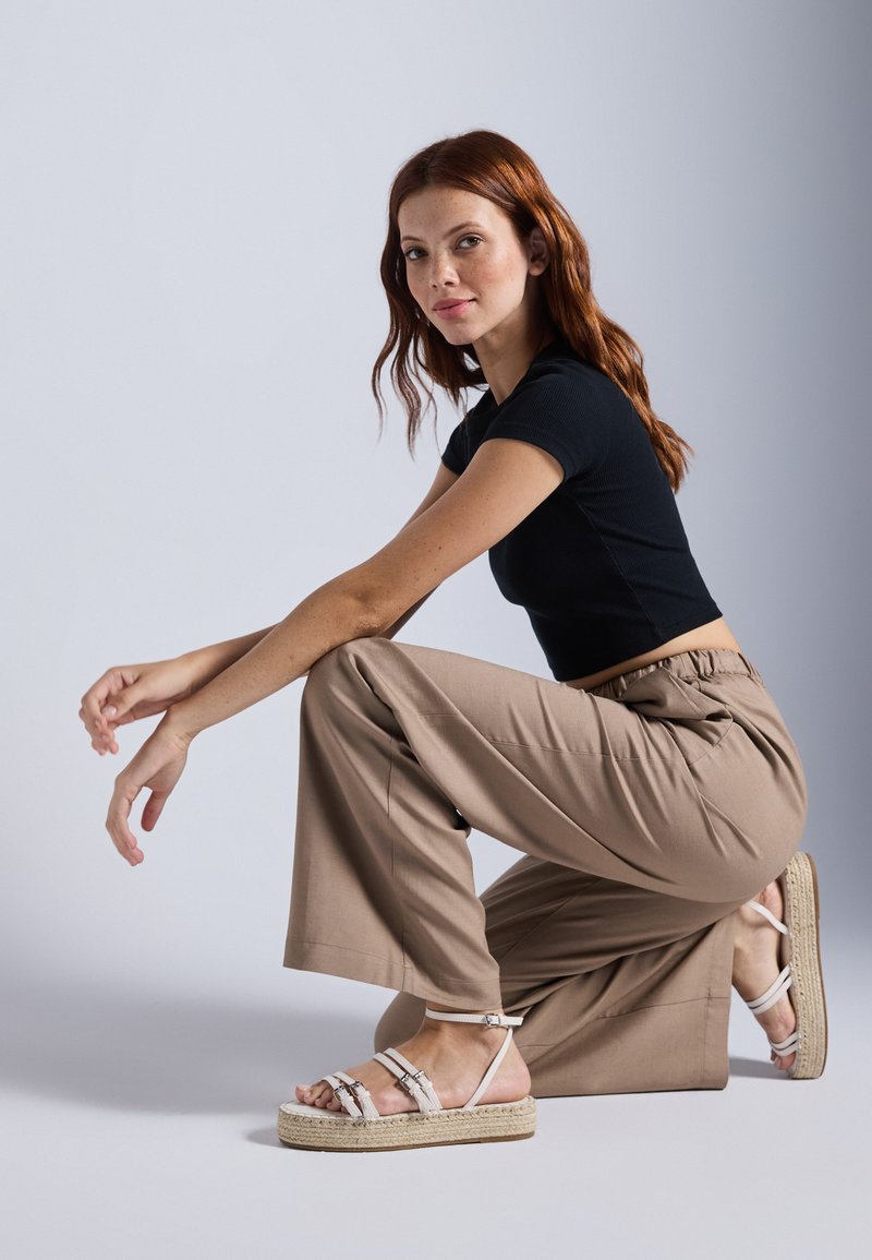 Top corto de rayas negras, pantalones de pierna ancha en color beige y alpargatas blancas con tiras y suela de yute trenzada, sobre un fondo claro.
