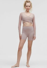 Dugulji dugih rukava, crossover crop top i kratke hlače visoka struka, oboje od mekog nude materijala s glatkom teksturom i prilagodljivim dizajnom.