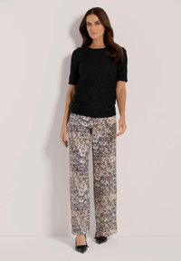 Zwart textuur top met korte mouwen, gecombineerd met lichtgepatenteerde, wijde broek in neutrale tinten en zwarte, puntige hakken.