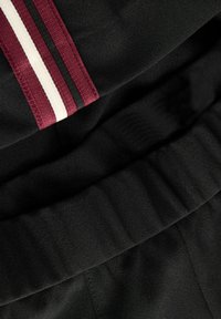 Crna tkanina glatke teksture s prugastim naglascima u bordo, crnoj i bijeloj boji. Sadrži detalj nabrane pojase.