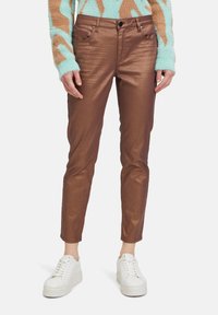 Braune, glänzende Leggings mit Slim-Fit und subtiler Glanz. Fünf-Taschen-Design mit Metallakzenten, kombiniert mit weißen Sneakers.