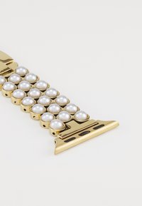 Pulsera en tono dorado que presenta perlas falsas blancas en un diseño agrupado. Incluye un cierre con orificios de ventilación para un ajuste seguro.