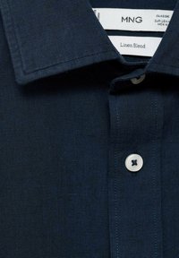 Námornícka košeľa z ľanovej zmesi s ostrým golierom, jedným gombíkom a textúrovanou látkou. Štítok hovorí "MNG Classic."