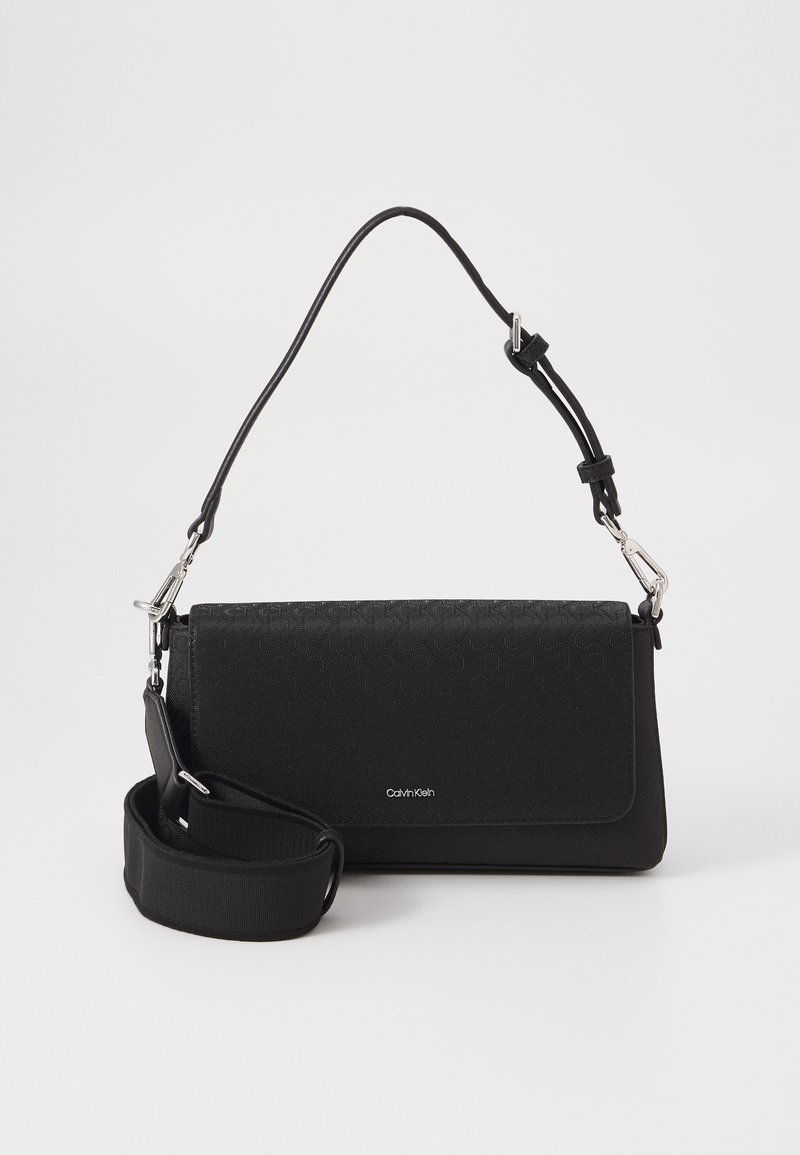 Sac à bandoulière noir Calvin Klein avec sangle réglable et fermeture à rabat sur fond blanc uni.