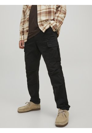 Pantalons cargo noirs avec poches latérales, fabriqués en tissu durable. Associés à une chemise à carreaux beige et des chaussures marron clair.