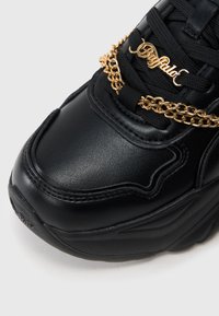 Μαύρο δερμάτινο αθλητικό παπούτσι με μαξιλαρωτό γιακά, υφή στην επιφάνεια και διακοσμητική χρυσή αλυσίδα πάνω από τα κορδόνια. Διαθέτει ανθεκτική σόλα από καουτσούκ.