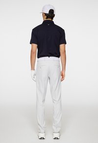 Merenkukka-paita, valkoinen vyö, vaaleanharmaat housut ja valkoinen lippalakki. Hanskat vasemmassa kädessä. Sileä kangas, istuva malli ja suora lahkeiden muotoilu.