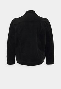 Chaqueta de pana negra con una textura suave, mangas largas, un cuello y un corte recto con detalles de canalé vertical en la parte posterior.