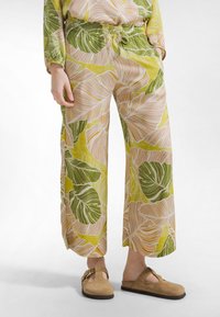 Pantalones ligeros de pierna ancha en tejido amarillo con estampado de hojas verdes. Presentan una cintura elástica con cordón y aberturas laterales.