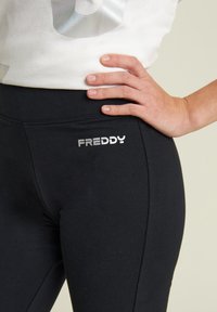 Leggings neri elasticizzati realizzati in tessuto liscio, con il logo argentato "FREDDY" sulla vita, dal design aderente.