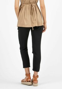Black tapered pants with rolled cuffs, paired with tan strappy wedge sandals and a loose beige top cinched at the waist with a tie.