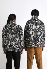 Faux fur jackets with abstract black, white, and gray patterns. High collars, loose fit, and textured surface. Two models with distinct hair.