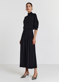 Pull col roulé noir à côtes associé à un pantalon large taille haute plissé noir et des escarpins à dos zèbre.