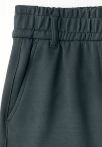 Pantalons de survêtement gris foncé avec une texture lisse, une taille élastique et des poches latérales. Le tissu a un léger éclat et est léger.