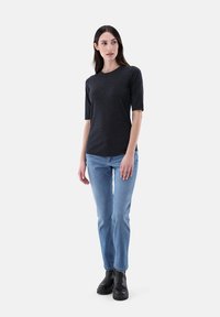 Dunkelgraues Kurzarmoberteil mit rundem Halsausschnitt, kombiniert mit hellblauen Jeans und schwarzen Knöchelstiefeln, vor einem schlichten weißen Hintergrund.