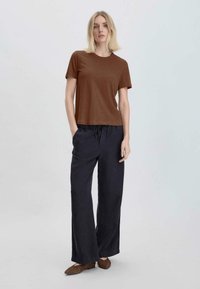 T-shirt marrone a maniche corte abbinato a pantaloni blu navy larghi. I pantaloni presentano un elastico in vita e tasche laterali. Ballerine marroni completano il look.