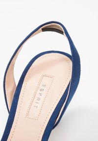 Gros plan sur une sandale à bride arrière en daim bleu marine avec une semelle intérieure beige et le logo Esprit embossé sur la semelle.