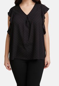 Black blouse with short ruffled sleeves, V-neckline, and red polka dots. Lightweight fabric with a relaxed fit and a tie detail at the front.