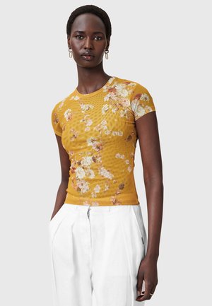 Top fitted a maniche corte con stampa floreale gialla e scollatura rotonda, realizzato in un tessuto leggero e strutturato.