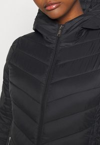 Gros plan sur une personne portant une veste noire rembourrée avec un col montant zippé et des coutures diagonales matelassées.