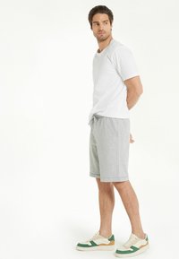 Pantalones cortos grises con cinturilla elástica, combinados con una camiseta de cuello redondo blanca y deportivas multicolores. Tejido de algodón suave.