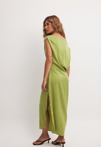 Ilgas žalias satino suknelė, pasižyminti laisvu siluetu, be petnešėlių dizainu ir šoniniais įpjovimais. Nešiojama su juodais sandalais. Lygus paviršius.