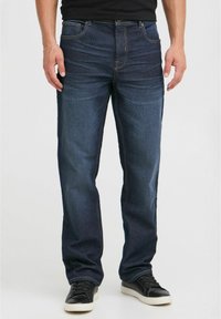 Vaqueros de mezclilla azul oscuro con corte recto, que cuentan con cinco bolsillos y costuras sutiles. Llevados con zapatillas bajas negras.