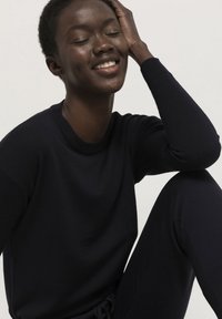 Marineblauer Strickpullover mit Rundhalsausschnitt und langen Ärmeln, der eine glatte Textur und eine lockere Passform aufweist. Modell sitzt und lächelt.