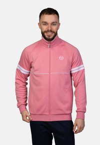 Rosa Zip-Up Sweatshirt mit hohem Kragen, weißen Streifen an den Ärmeln und einem Logo auf der Brust. Verfügt über eine glatte Stoffoberfläche.