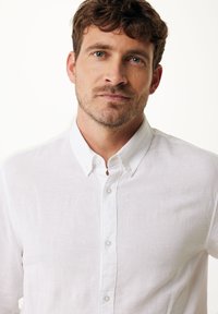 Witte linnen overhemden met kraag, voorzien van een iets gestructureerde stof en een klassieke knoopsluiting aan de voorkant.